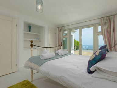 A bedroom with a bed and rolled towels near glass doors overlooking a patio and sea view at Moonbeams in Carbis Bay