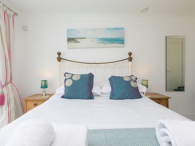 A bedroom with a double bed two teal pillows two wooden bedside tables with lamps a wall mirror and a painting of a beach scene at Moonbeams in Carbis Bay