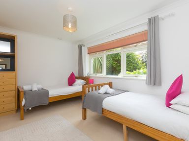 A bedroom with two single wooden beds with white bedding and pink pillows at Moonbeams in Carbis Bay
