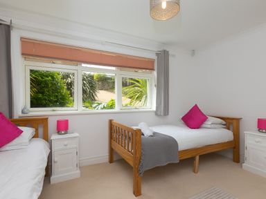 A bedroom with two single wooden beds with white bedding and pink pillows at Moonbeams in Carbis Bay