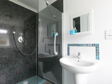 A bathroom with a glass shower enclosure a white pedestal sink a mirror cabinet and tiled wall at Moonbeams in Carbis Bay