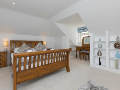 A bedroom with a wooden bed and bedside tables with lamps a dressing table and built in shelves with decorative items at Moonbeams in Carbis Bay
