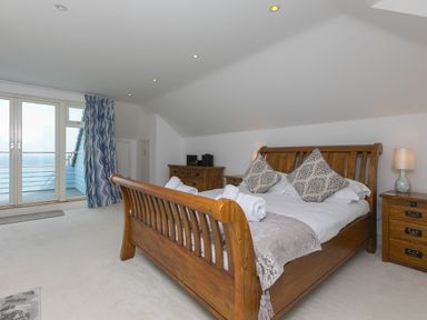 A bedroom with a wooden bed and bedside tables next to glass doors with blue patterned curtains at Moonbeams in Carbis Bay