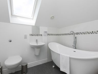 A bathroom with a white toilet wall-mounted sink and freestanding bathtub under a skylight at Moonbeams in Carbis Bay