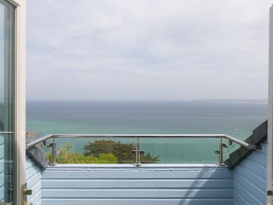 A balcony with a glass and metal railing overlooking the ocean and distant coastline at Moonbeams in Carbis Bay