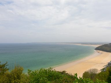 A view of a sandy beach with the sea and distant coastline at Moonbeams in Carbis Bay