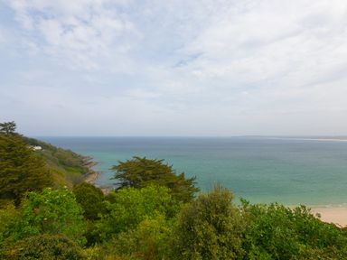 A coastal landscape with green trees and a sandy beach next to the sea at Moonbeams in Carbis Bay