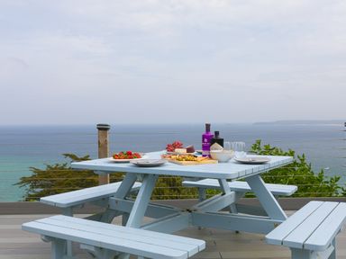 An outdoor picnic table with plates food bottles and glasses overlooking the sea at Moonbeams in Carbis Bay