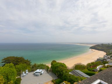A beach view with a wooden deck and white chairs overlooking the ocean at Moonbeams in Carbis Bay