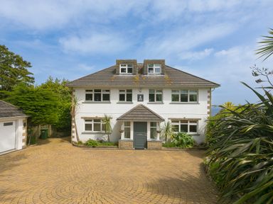 A front view of a two-story house with dormer windows and a tiled roof surrounded by plants and trees at Moonbeams in Carbis Bay
