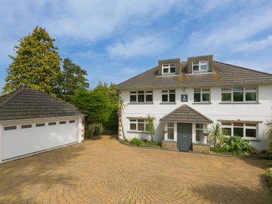 A white two story house with a grey door and dormer windows next to a detached garage with a paved circular driveway at Moonbeams in Carbis Bay