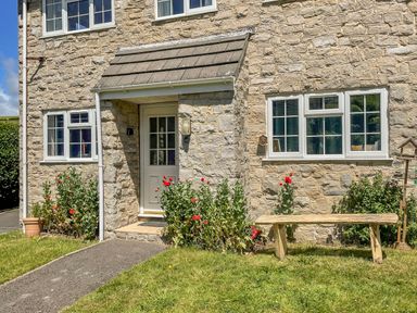 Stone house front with a small porch door red flowers near windows and a wooden bench at West Lulworth Apartment in West Lulworth