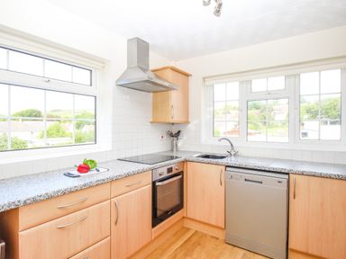 A kitchen with wooden cabinets a dishwasher an oven a stovetop a sink and windows with outdoor views at West Lulworth Apartment in West Lulworth