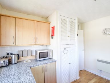 A kitchen corner with wooden cabinets a microwave kettle toaster and storage containers at West Lulworth Apartment in West Lulworth