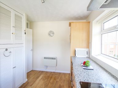 A kitchen with white cabinets wooden floor a clock on the wall and a countertop with vegetables and a chopping board at West Lulworth Apartment in West Lulworth