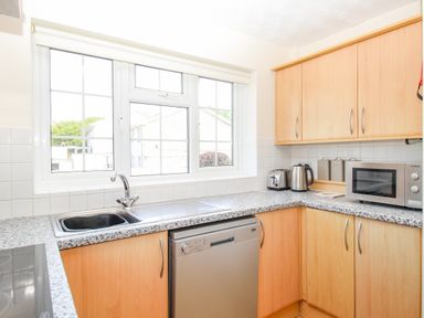 A kitchen with wooden cabinets a window a sink a dishwasher a toaster a kettle and a microwave at West Lulworth Apartment in West Lulworth