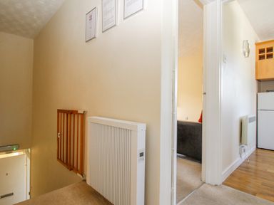 A hallway with a wooden safety gate and a white radiator leading to a kitchen and living area at West Lulworth Apartment in West Lulworth