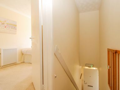 A view of a hallway with a door leading to a bedroom and stairs leading down to a white entrance door at West Lulworth Apartment in West Lulworth