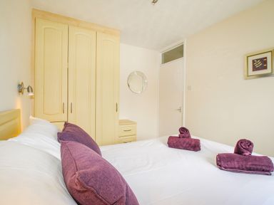 A bedroom with a bed with purple pillows and towels next to a wooden wardrobe and a door at West Lulworth Apartment in West Lulworth