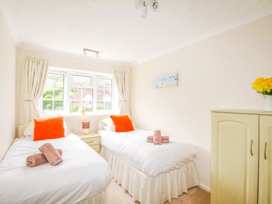 A bedroom with two single beds with orange pillows and folded towels next to a window at West Lulworth Apartment in West Lulworth