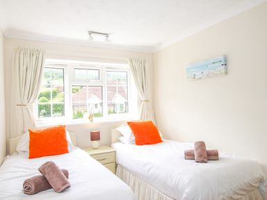 A bedroom with two single beds with orange pillows and rolled towels at West Lulworth Apartment in West Lulworth