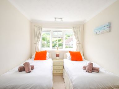 A bedroom with two single beds with orange pillows and rolled towels next to a window at West Lulworth Apartment in West Lulworth