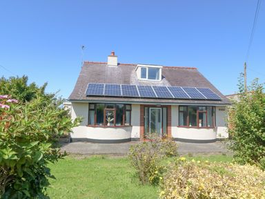 A house with solar panels on the roof and a green garden in front at Awelfryn in Elim near Llanddeusant