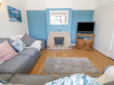 A living room with a fireplace a television on a wooden cabinet and grey sofas at Awelfryn in Elim near Llanddeusant