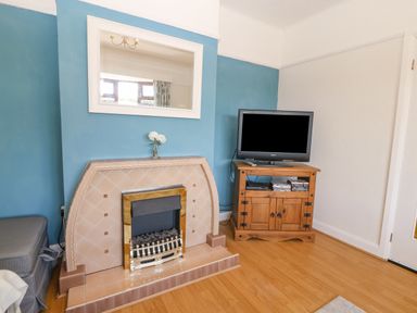 A living room with a tiled fireplace a wall mirror a small wooden cabinet with a television and a vase with flowers at Awelfryn in Elim near Llanddeusant