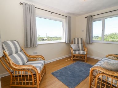 A sitting room with wicker chairs and a blue rug at Awelfryn in Elim near Llanddeusant