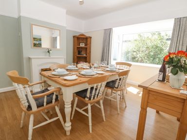 A dining room with a wooden table set for six near a large window at Awelfryn in Elim near Llanddeusant