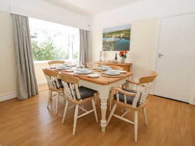 A dining room with a wooden table set for six and chairs near a window at Awelfryn in Elim near Llanddeusant