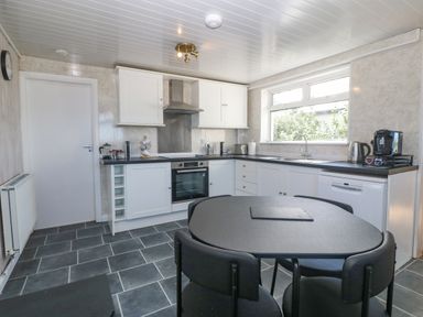 A kitchen with white cabinets black countertops a dining table with chairs and appliances at Awelfryn in Elim near Llanddeusant