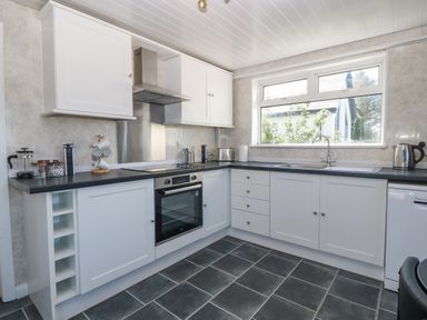 A kitchen with white cabinets a black countertop a window oven and various appliances at Awelfryn in Elim near Llanddeusant