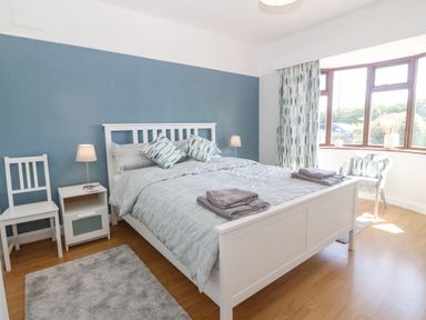A bedroom with a white bed blue accent wall bedside table lamps chair and large window at Awelfryn in Elim near Llanddeusant
