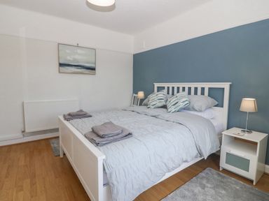 A bedroom with a white bed frame blue bedding bedside tables with lamps and a painting on the wall at Awelfryn in Elim near Llanddeusant