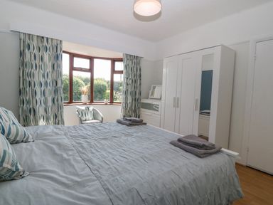 A bedroom with a bed pillows folded towels wardrobe chair and bay window at Awelfryn in Elim near Llanddeusant