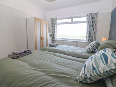 A bedroom with two single beds green bedding a wardrobe and patterned curtains at Awelfryn in Elim near Llanddeusant