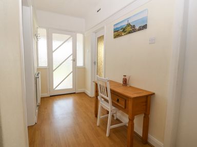 A hallway with a wooden floor a wooden table and a white chair near a glass door at Awelfryn in Elim near Llanddeusant