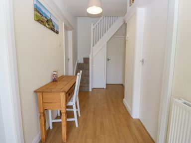 A hallway with wooden flooring a wooden table and white chair a staircase and multiple doors at Awelfryn in Elim near Llanddeusant