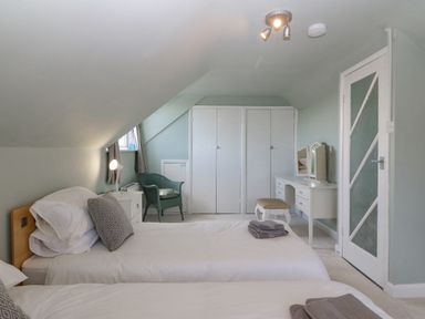 A bedroom with two single beds a green chair a white dresser with mirror and a white wardrobe at Awelfryn in Elim near Llanddeusant