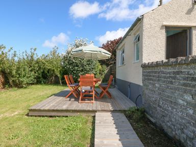A wooden deck with a table and chairs under an umbrella beside a small building at Awelfryn in Elim near Llanddeusant
