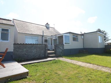 The back of a single story house with a small brick wall patio and a grassy garden at Awelfryn in Elim near Llanddeusant