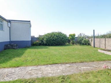 A garden with a grass lawn a paved pathway shrubs and a white house on the left at Awelfryn in Elim near Llanddeusant