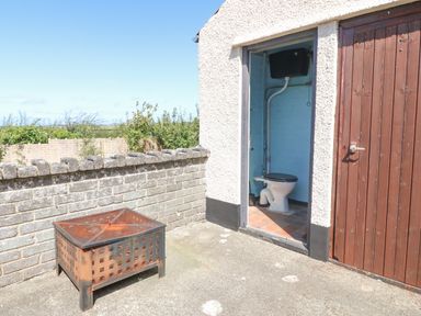 An outdoor area with a brick wall and a metal fire pit next to an open door showing a toilet at Awelfryn in Elim near Llanddeusant
