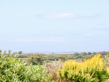 A rural landscape with green bushes and fields under a blue sky at Awelfryn in Elim near Llanddeusant