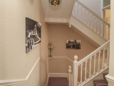 A staircase with white railings and striped carpet with photos on the walls at Lonsdale Villa in Scarborough