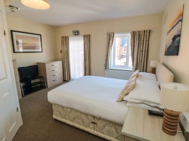 A bedroom with a double bed two bedside tables with lamps a TV on a stand and a chest of drawers at Lonsdale Villa in Scarborough