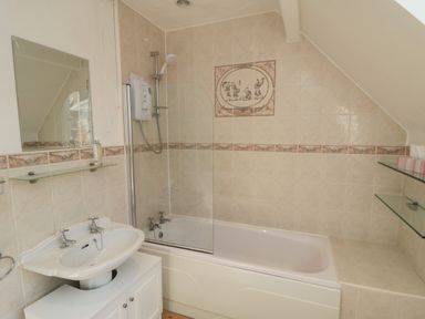 A bathroom with a bathtub shower combo a sink with cabinet and mirror at Lonsdale Villa in Scarborough