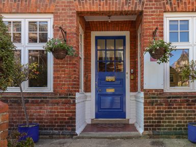 A blue front door with a welcome sign framed by red brick walls and windows with hanging flower baskets at Lonsdale Villa in Scarborough